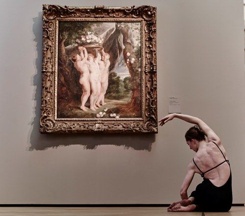 Jamie shown facing away from view, reclined on one hip, sitting in front of a painting.